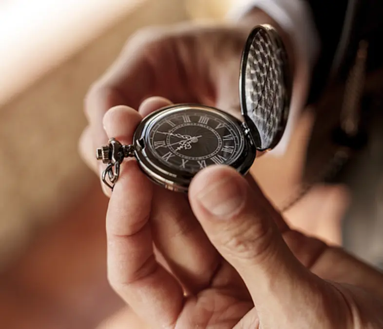 Close-up of hands holding an open vintage pocket watch.