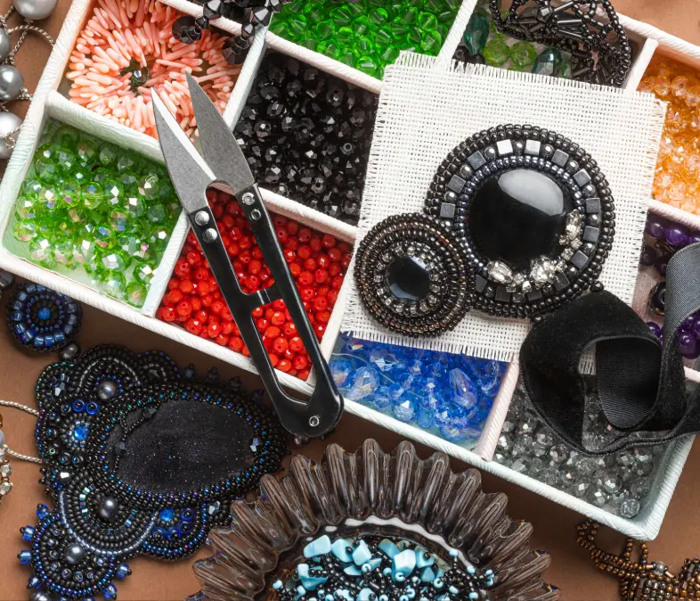 Beaded jewelry making supplies including beads, pliers, and thread.